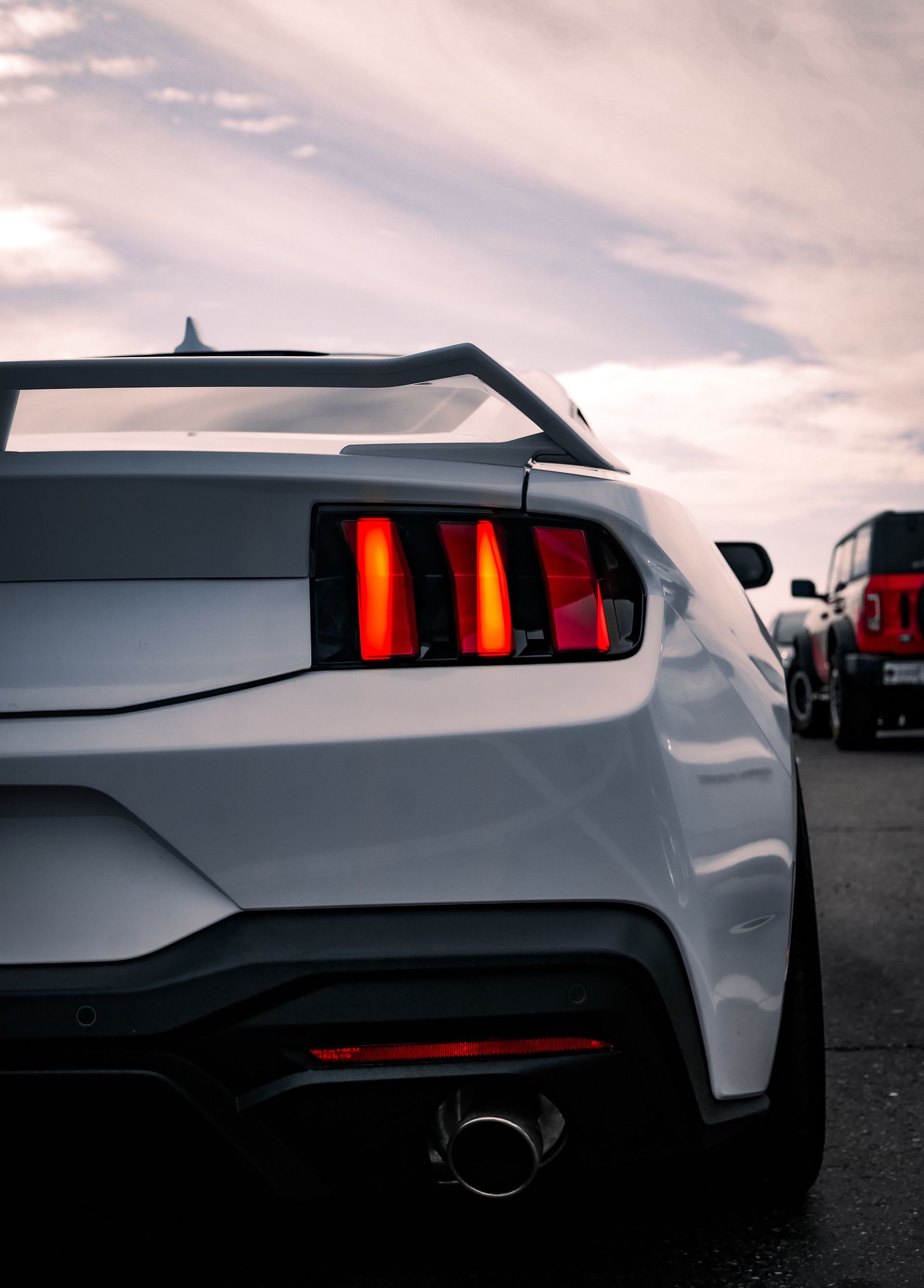 A sleek white sports car with illuminated taillights, captured from behind against a scenic sunset backdrop.